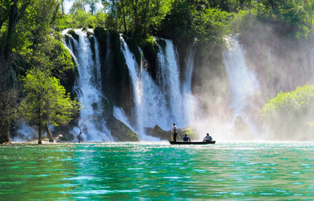 A beautiful waterfall flowing into the river with people admiring it from a boatの写真素材