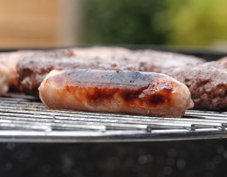 A closeup shot of sausages and burger pattie on the grillの写真素材
