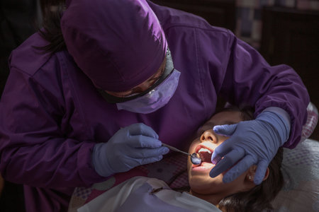 A closeup of a Mexican female dentist examining doing teeth check up on a young girlの写真素材