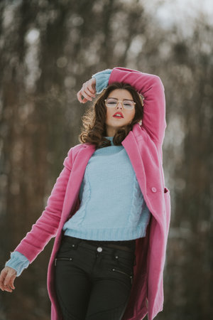 A young Caucasian female wearing a blue shirt and a pink coat posing in a parkの写真素材