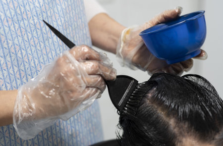 A hairdresser with single-use plastic gloves dying a woman's hair roots with a hairbrushの写真素材