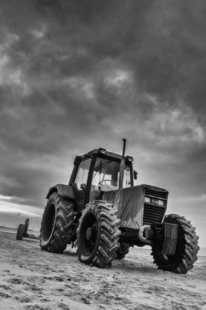 A vertical grayscale shot of a tractor and a cloudy dark skyの写真素材