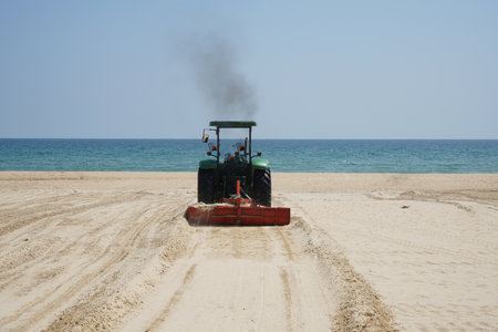 A back view of a tractor cleaning on a sandy beachの写真素材