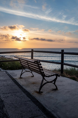 A vertical shot of a wooden bench on the beach at sunriseの写真素材