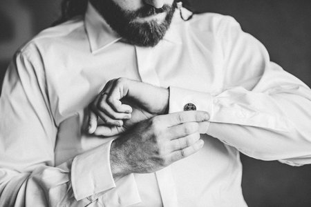 A grayscale shot of a man buttoning his shirt cuffsの写真素材