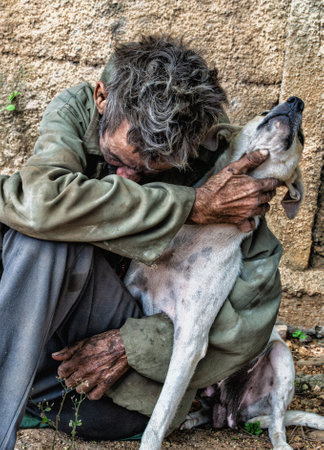 A sad homeless Cuban man sitting in front of a brick wall, embracing a dogの写真素材