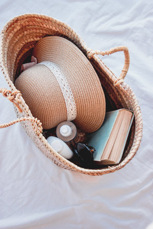 A vertical shot of a straw bag with straw hat, sun cream, a book, and sunglassesの写真素材