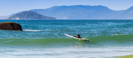 A young woman surfing on the beach with mountains in a backgroundの写真素材