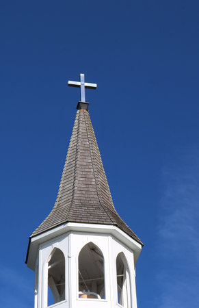 A church steeple roof with a shiny metal cross against the blue sky