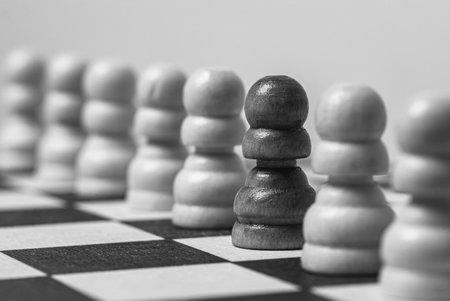 A selective focus shot of the black pawn among the white pawns on the chessboard