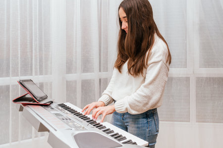A Spanish female using her tablet while playing on a digital pianoの写真素材