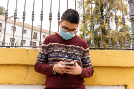 Stock photo of young boy wearing face mask due to covid19 using his mobile phone in the park.の写真素材
