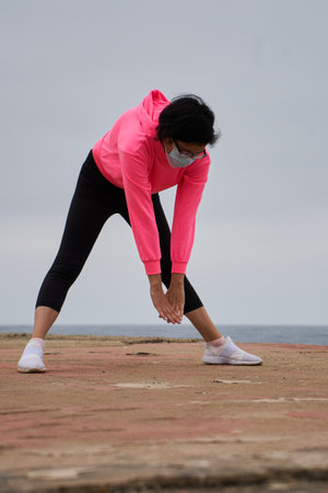 A Chilean woman with a mask stretching in front of the sea - New normality, sport during pandemic