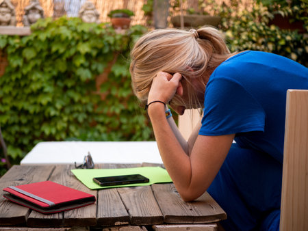 An adult depressed blonde woman hunched over on her hands sitting in the gardenの写真素材