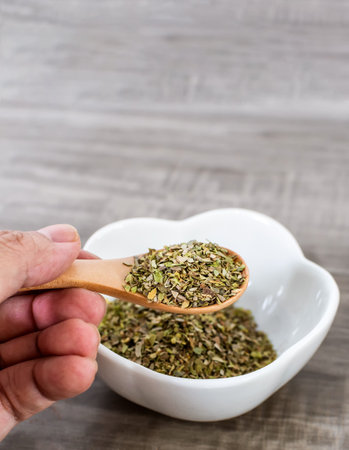 A closeup of a hand holding a wooden spoon  with oreganoの写真素材