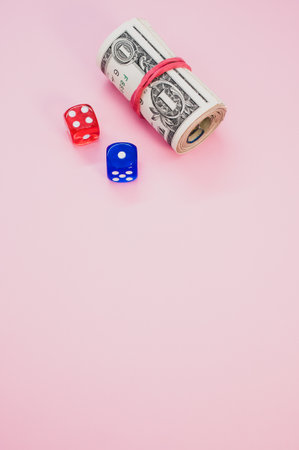 A vertical shot of a roll of dollars and dice isolated on pink background for a copy spaceの写真素材