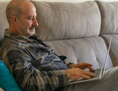 man watching pc and paying online, drinking coffee in the living room of his homeの写真素材