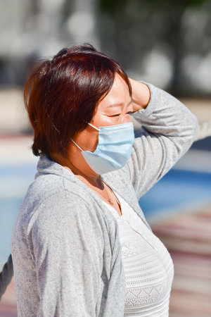 A vertical shot of an Asian female in a medical mask enjoying the sunshine outdoorsの写真素材