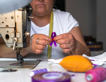 A shallow focus of an adult Spanish female sewing a purple ribbon on a facemask - COVID-19 awarenessの写真素材