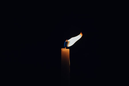 A clsoeup shot of a lit candle with its flame deviated from the wind isolated on black backgroundの写真素材