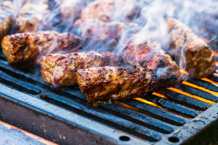 A closeup of hand preparing meat rolls called mici or mititei on barbecue with rising smokeの写真素材