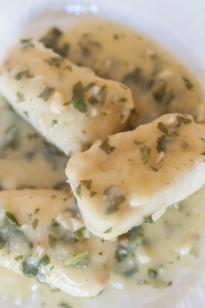 A vertical shot of a bowl of delicious cooked hake with sauce, garlic, and parsley