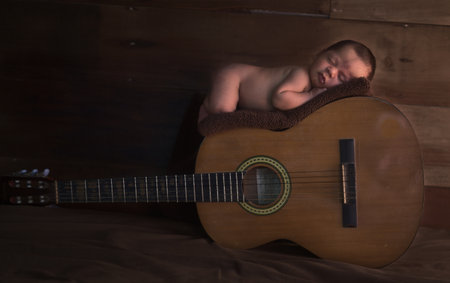 A cute male newborn baby sleeping on a blanket on a guitarの写真素材