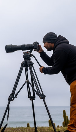 vertical photo of a nature photographer with his camera and telephoto to take photos of surfing ocean in the backgroundの写真素材
