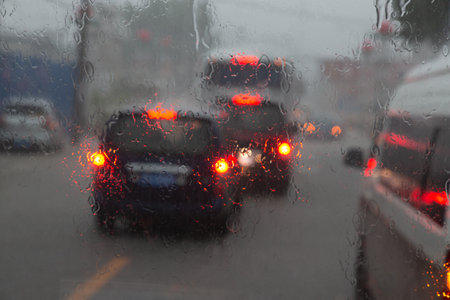 A rain-soaked car window with a road visible behind it and cars with their hind lights onの写真素材