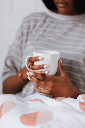 A young African female drinking a cup of coffee or tea while lying in bed after waking up in the morningの写真素材
