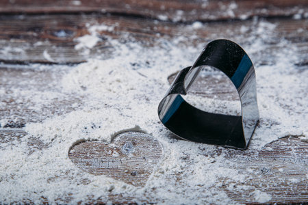 A closeup shot of a heart-shaped cookie cutter and flour scattered on the kitchen table with copy spaceの写真素材