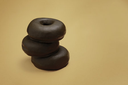 A closeup shot of piled chocolate donuts isolated on a brown backgroundの写真素材