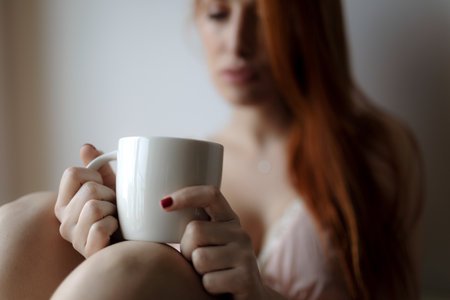 A closeup shot of a beautiful Caucasian ginger female holding a coffee cupの写真素材
