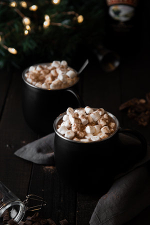 A vertical shot of two black cups with hot drink with marshmallows on a wooden tableの写真素材