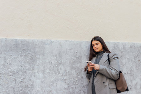 A beautiful Caucasian female using her smartphone while leaning on the wallの写真素材