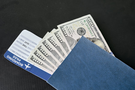 A closeup of the hundred dollar bills in the passport with a ticket on the black surface