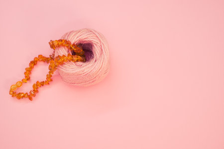 A closeup shot of an amber beads necklace and a cotton yarn on a pink surfaceの写真素材