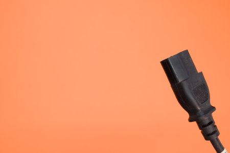 A closeup shot of a black power cord on an orange background