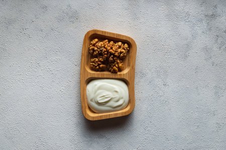 A top view of mayo and walnuts on a wooden plate on a white surface