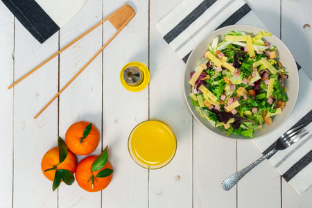 A plate of fresh Mediterranean salad with olive oil served with orange juice on a white wooden tableの写真素材