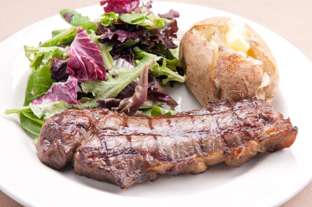 grilled new york strip steak with salad and baked potatoの写真素材