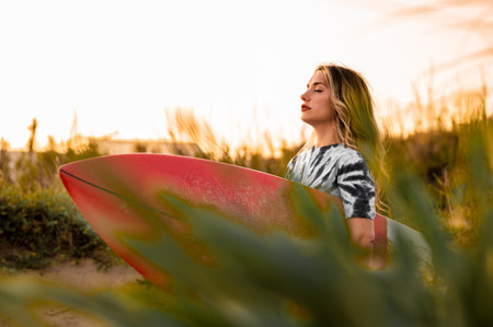 A young blonde female surfer walking with her surfing board at the beach