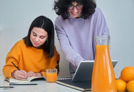 A view of two young women looking at something on the tablet on the table with fruits and juice