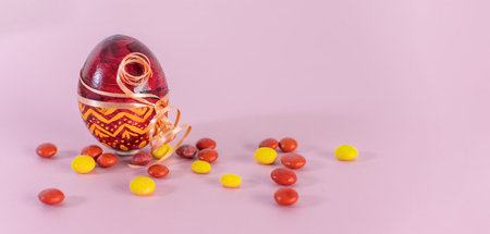 A close-up shot of a red easter egg and candies on a pink background.