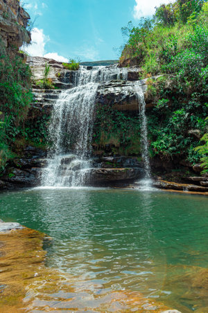 A beautiful vertical shot of a waterfall in a jungle with bright blue sky and greeneryの写真素材