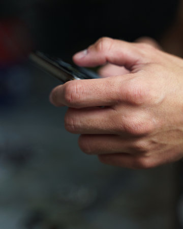 A shallow focus of male hands using a mobile phone against a blurred backgroundの写真素材