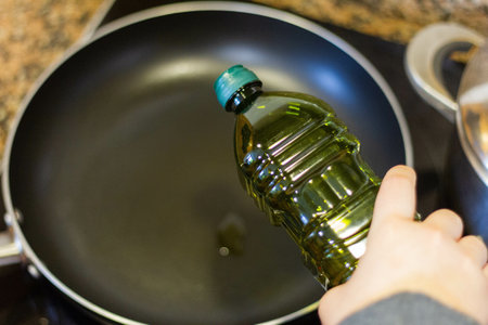 A closeup shot of the hand of a girl pouring oil in a pan