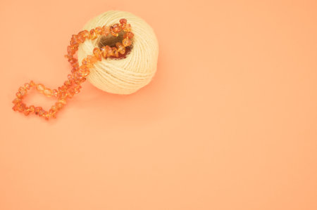 A closeup shot of an amber beads necklace and a cotton yarn on an orange surfaceの写真素材