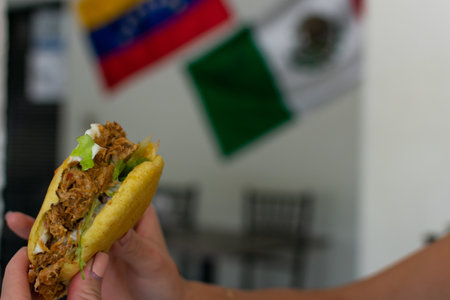A delicious arepa held by a person holding it with his hands. in a restaurant with the background of the mexican and venezuelan flag.の写真素材