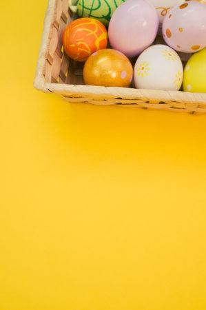 A woven basket filled with colorful Easter eggs on yellow backgroundの写真素材